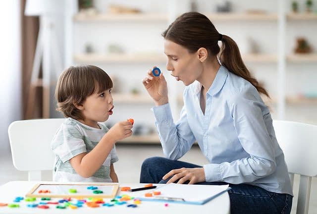 A therapist doing a speech therapy exercise with a young child at a table